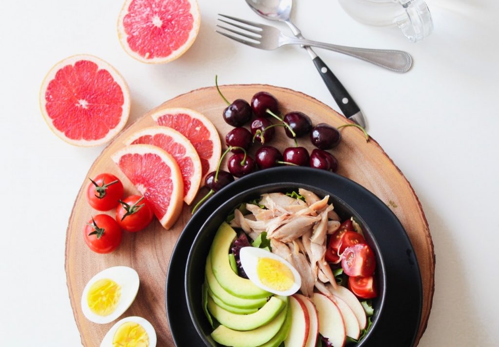 buddha bowl avocat oeuf tomate sur support en bois avec pamplemousse et cerises à côté