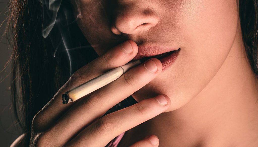 Jeune femme qui fume une cigarette malgré les risques de problèmes dentaires